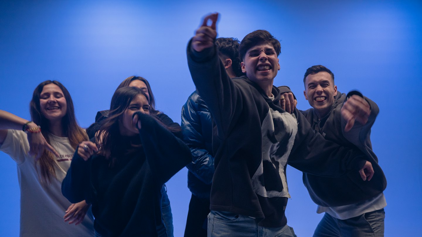 Five people in casual clothing laugh and gesture with excitement.